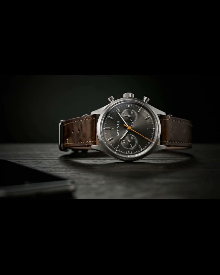 A steel chronograph watch with a leather strap on a dark surface